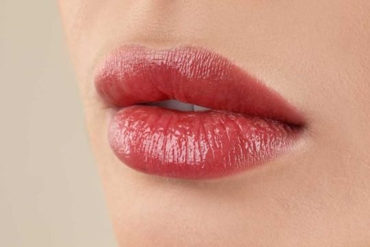 Woman with beautiful perfect lips after permanent makeup procedure on beige background, closeup